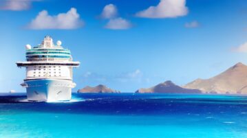 Un bateau de croisière naviguant sur les eaux turquoise des Caraïbes avec un ciel bleu et des îles en arrière-plan.
