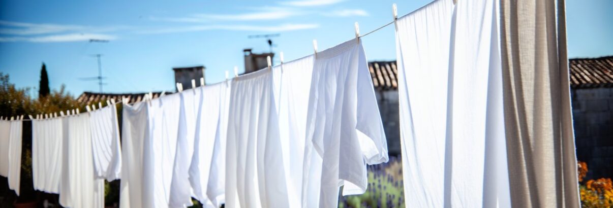 Des draps blancs fraîchement lavés et étendus pour sécher à l'extérieur, suspendus à une corde à linge sous un ciel bleu.