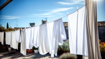 Des draps blancs fraîchement lavés et étendus pour sécher à l'extérieur, suspendus à une corde à linge sous un ciel bleu.