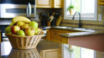 Une panière remplie de pommes et de bananes posée sur le plan de travail d'une cuisine lumineuse.